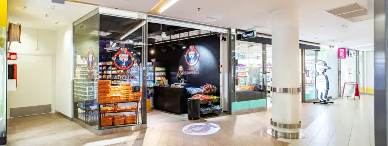 Amerikkalaistyylinen kioski käytävällä, karkkia ja juomia myynnissä, Hello America -logo seinällä.