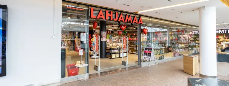 LAHJAMAA lahjakauppa lasiseinän edessä, punaiset logot ja sisällä täynnä lahjatavaroita.