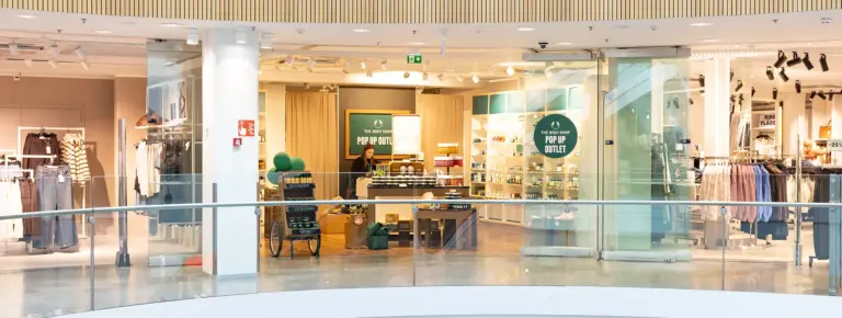 Kauppakeskuksen vaatekauppa lasiseinillä; myyjä kassalla, vasemmalla ja oikealla vaatteita, POP UP OUTLET -kyltti.